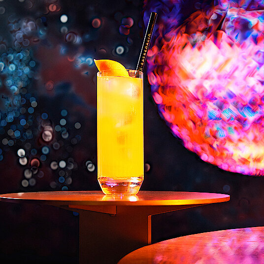 Langes Longdrinkglas mit einem fruchtig-orangenem Cocktail gefüllt – im Raum "Ocean" bei Eatrenalin Late Night.