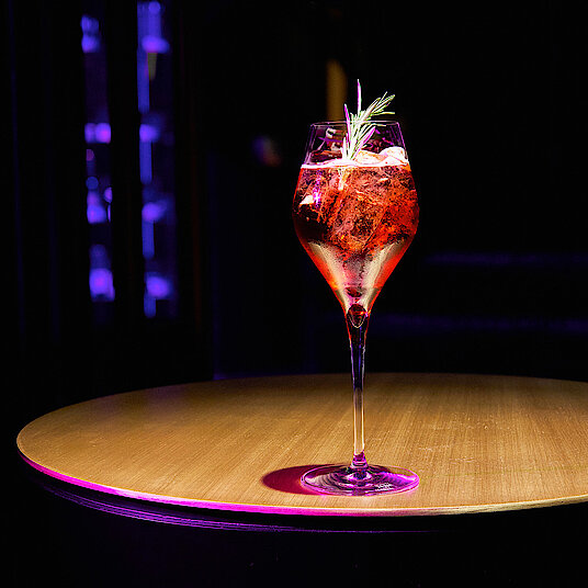 Ein hohes, gewölbtes Champagnerglas mit einem lecker-spritzigen Aperitif in der Lounge von Eatrenalin Late Night.